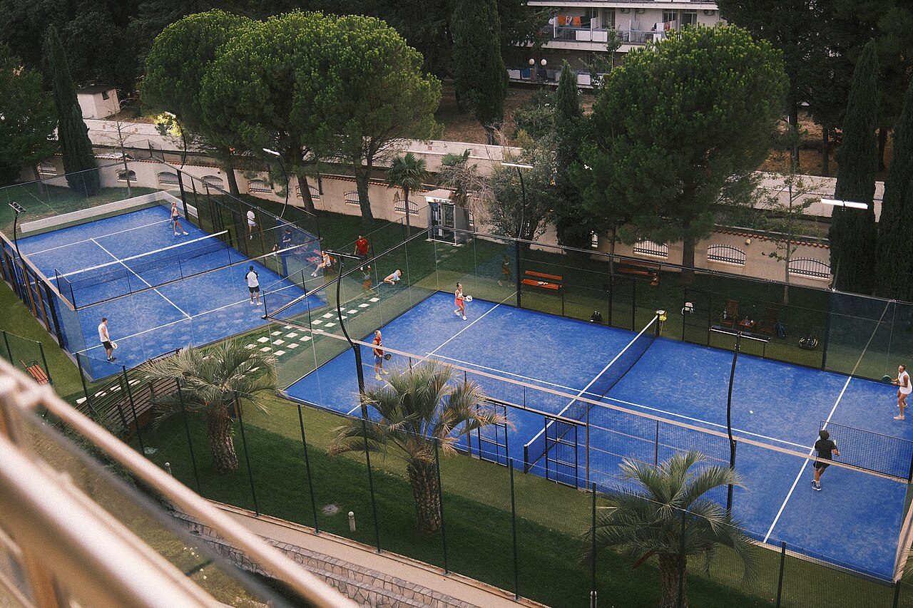 Spelers tijdens een padelwedstrijd op blauwe buitenbanen tussen het groen